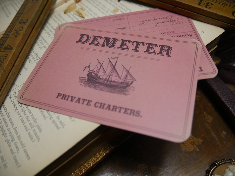 May include: A pink card with the text "DEMETER PRIVATE CHARTERS."  A black and white illustration of a sailing ship is in the center of the card.