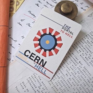 May include: A rectangular card featuring a graphic of a red and white octagonal shape with a blue and yellow center. The text reads THE PORTAL TO HELL, CERN TO HELL, and TRAVEL TO THE UNDERWORLD IN UNDER 3 HOURS in black, red, and blue ink.