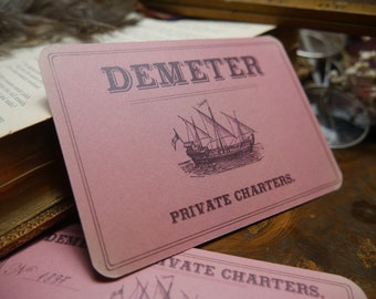 May include: A pink card with the text "DEMETER PRIVATE CHARTERS."  A black and white illustration of a sailing ship is in the center of the card.