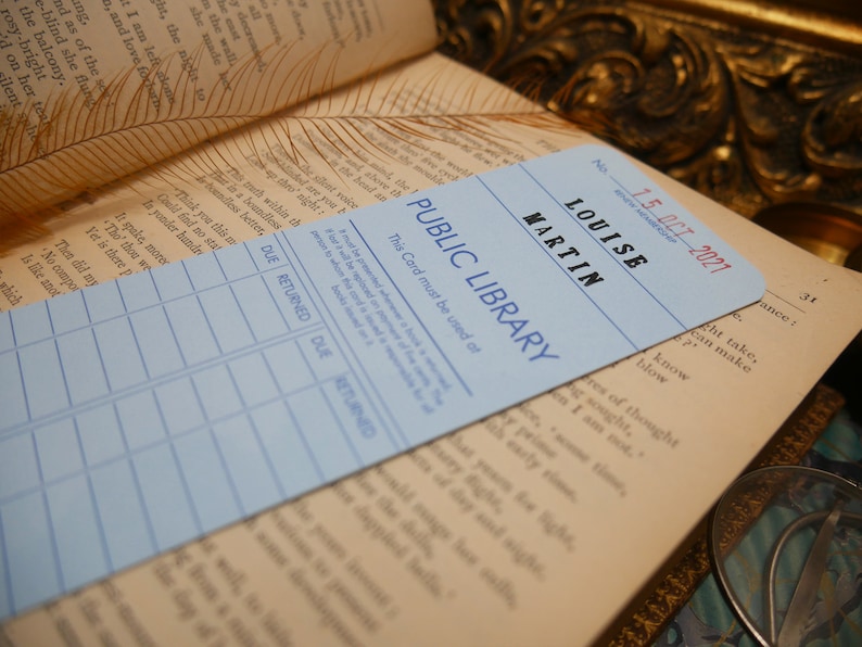 May include: A light blue library card with the text "PUBLIC LIBRARY" and "LOUISE MARTIN" printed in dark blue. The card has a date stamp that reads "15 OCT 2021". The card has a grid with the headings "DUE", "RETURNED", "DUE", and "RETURNED".