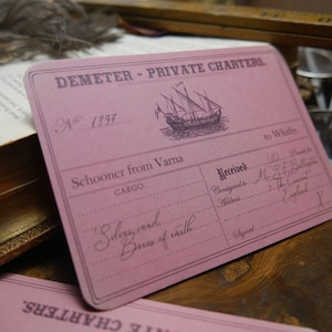 May include: A pink card with the text "DEMETER - PRIVATE CHARTERS."  The card has a number "N 1897" and the text "Schooner from Varna" and "CARGO." The card also has the text "to Whitby." and "Received."  The text "Consigned to" and "Address" are followed by handwritten text. The card has the text "Silky sand" and "Boxes of caith" written in cursive.