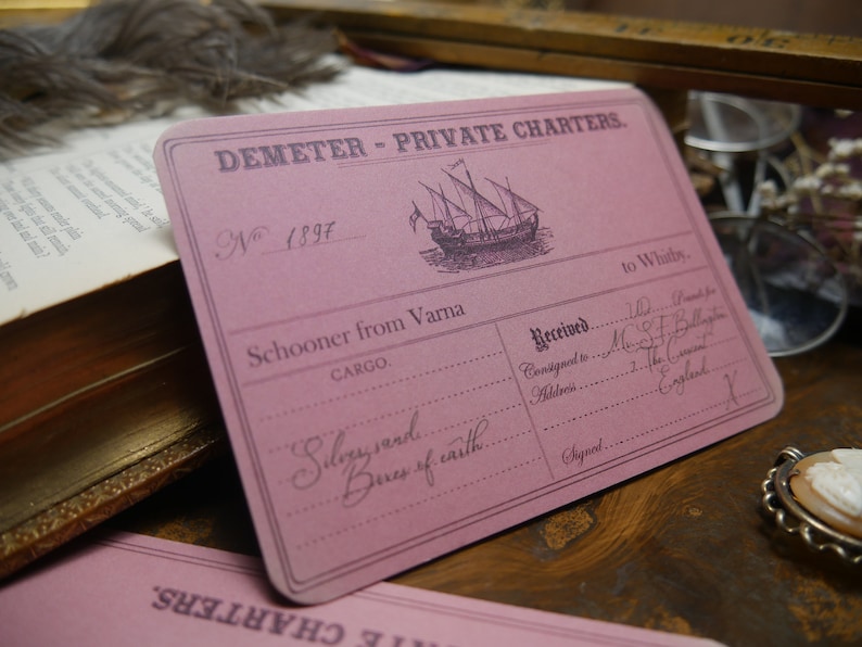 May include: A pink card with the text "DEMETER - PRIVATE CHARTERS."  The card has a number "N 1897" and the text "Schooner from Varna" and "CARGO." The card also has the text "to Whitby." and "Received."  The text "Consigned to" and "Address" are followed by handwritten text. The card has the text "Silky sand" and "Boxes of caith" written in cursive.