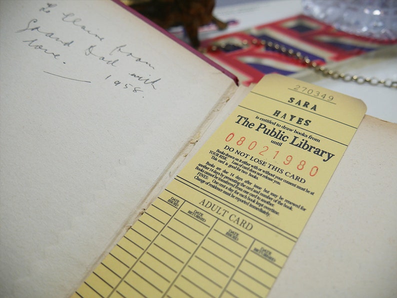 May include: A yellow library card with the text "SARA HAYES is entitled to draw books from The Public Library until 08021980" and the text "DO NOT LOSE THIS CARD". The card has a section for an adult card with columns for date, book, and author.