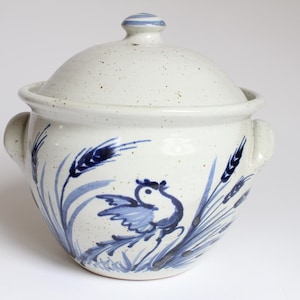 Könnte beinhalten: Weiße Keramik-Auflaufform mit einem blauen und weißen Design aus einem Vogel und Weizenähren. Die Form hat zwei Griffe und einen Deckel.
