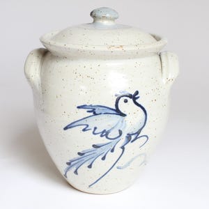 Könnte beinhalten: Ein Keramiktopf mit Deckel, mit einem handgemalten blauen Vogelmuster. Der Topf ist cremefarben mit gesprenkelten Details und hat zwei seitliche Griffe. Der Deckel hat einen kleinen Knopf. Ein dekorativer Küchenaufbewahrungsbehälter.