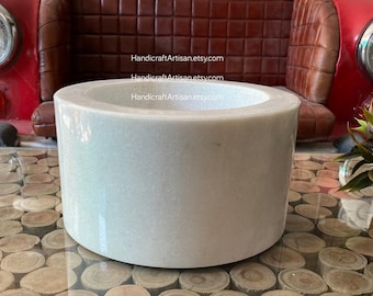 Pode incluir: Tigela de mármore branco com uma superfície lisa e redonda. A tigela está sobre uma mesa de madeira com tampo de vidro.