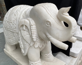 Puede incluir: Estatua de elefante de mármol blanco con tallas intrincadas y una trompa detallada. El elefante está de pie sobre una base cuadrada.