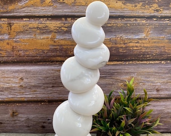 Puede incluir: Escultura de mármol blanco de esferas apiladas, que se asemeja a una torre. La escultura está sobre una base de mármol blanco y se exhibe sobre una superficie de madera.