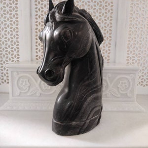May include: Black marble horse head sculpture. The sculpture is detailed with intricate lines and a realistic horse head.