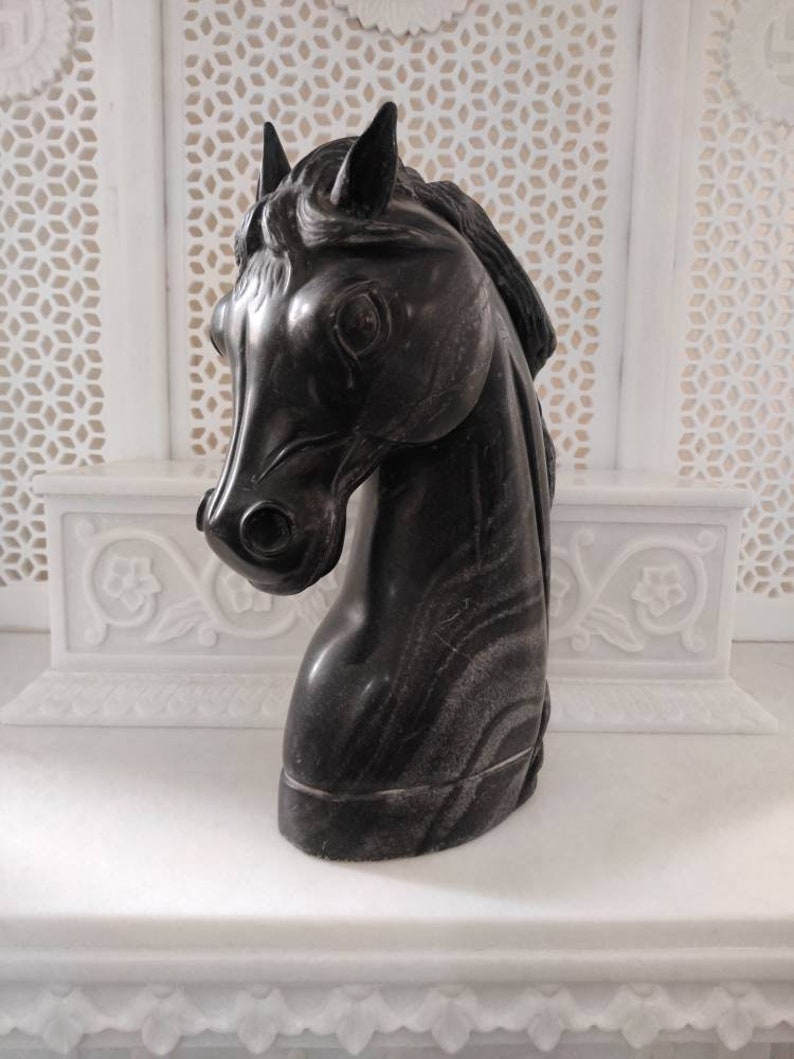 May include: Black marble horse head sculpture. The sculpture is detailed with intricate lines and a realistic horse head.
