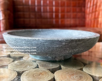 May include: A grey stone bowl with a smooth, rounded rim. The bowl is sitting on a wooden surface.