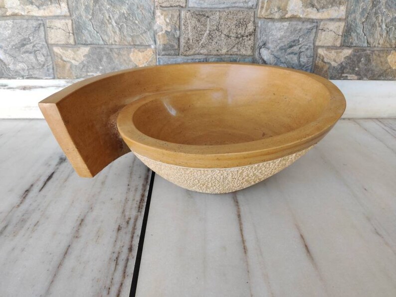 K&ouml;nnte beinhalten: Eine handgefertigte, hellbraune Steinschale mit einem einzigartigen Spiraldesign. Die Schale hat eine glatte Innenseite und eine strukturierte Au&szlig;enbasis. Die Schale misst ca. 38 cm lang, 25 cm breit und 10 cm tief.