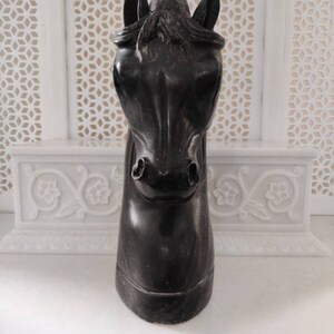 May include: Black horse head sculpture made of wood. The sculpture is carved in detail and has a realistic appearance.