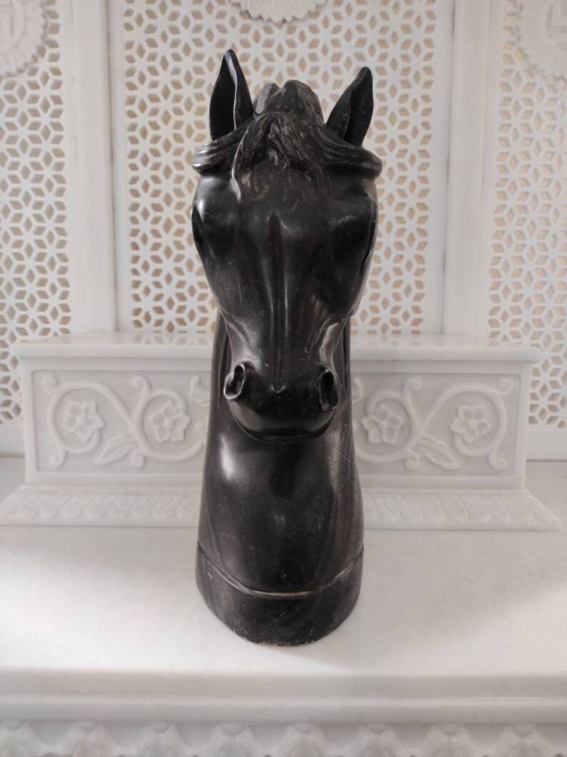 May include: Black horse head sculpture made of wood. The sculpture is carved in detail and has a realistic appearance.