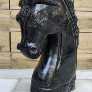 May include: Black marble horse head sculpture. The sculpture is detailed and realistic, with a smooth, polished finish.