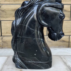 May include: A black marble sculpture of a horse's head. The sculpture is detailed and realistic, with a flowing mane and a strong, expressive face.
