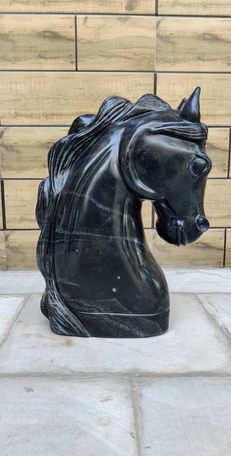May include: A black marble sculpture of a horse's head. The sculpture is detailed and realistic, with a flowing mane and a strong, expressive face.