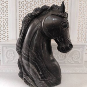 May include: Black marble horse head sculpture with a detailed mane and a striated pattern.