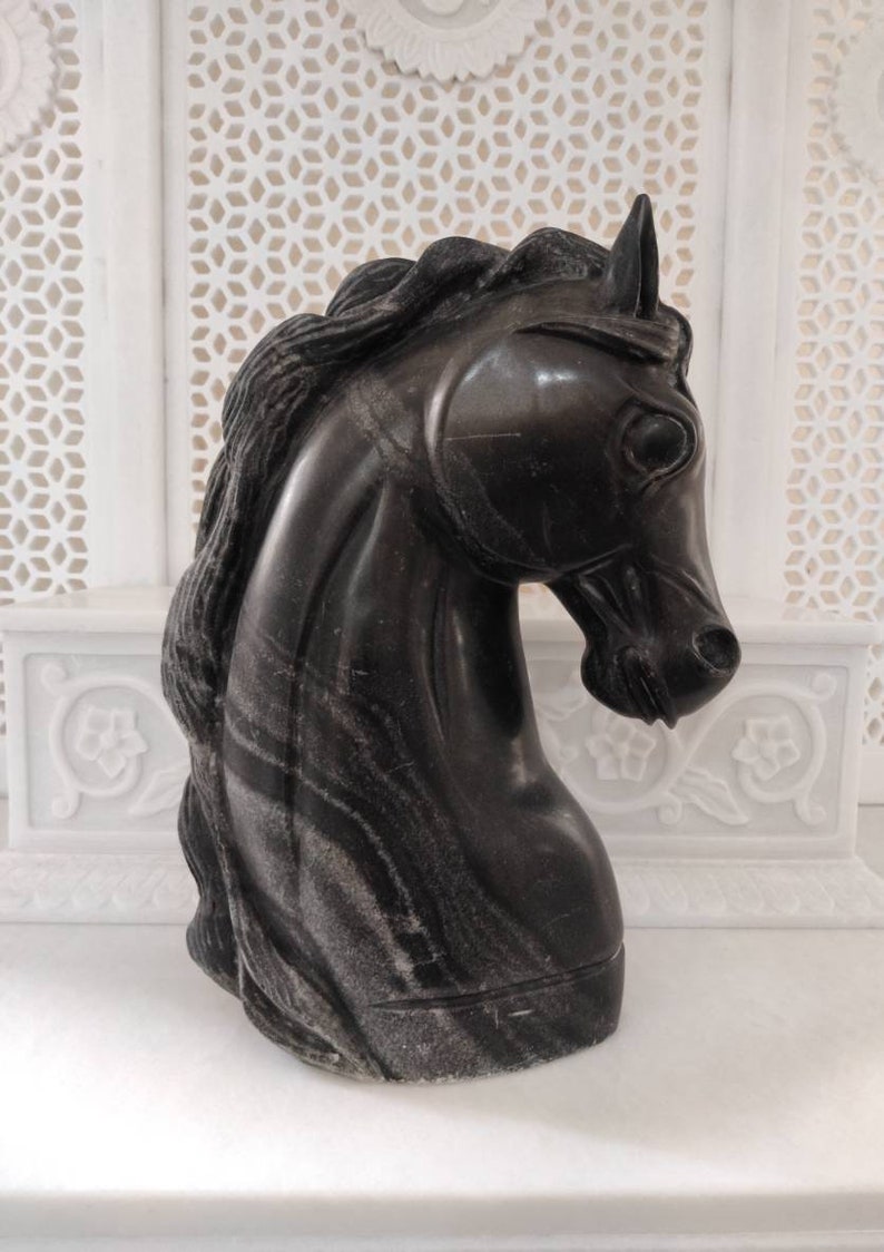 May include: Black marble horse head sculpture with a detailed mane and a striated pattern.
