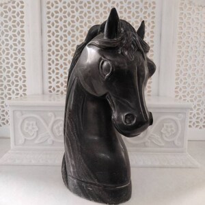 May include: Black marble horse head sculpture. The sculpture is detailed with a mane and has a smooth, polished finish.
