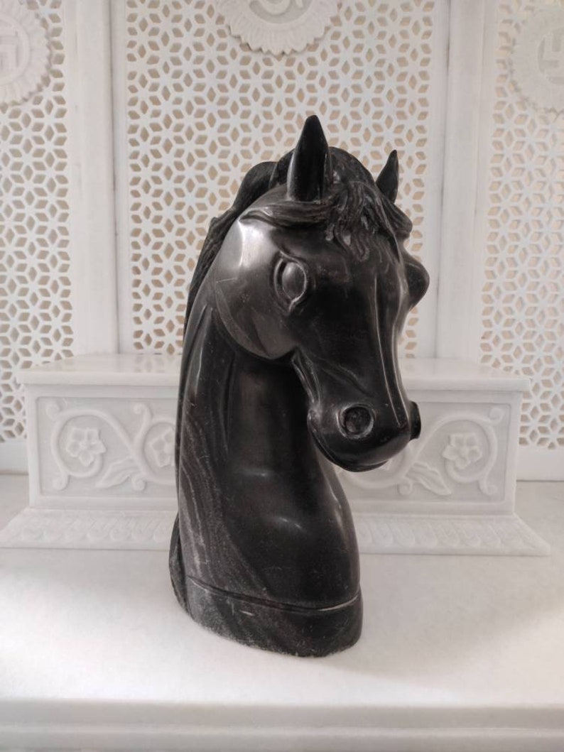 May include: Black marble horse head sculpture. The sculpture is detailed with a mane and has a smooth, polished finish.
