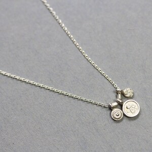 May include: A silver chain necklace with three silver charms. The charms are round and have different designs. The necklace is on a gray background.