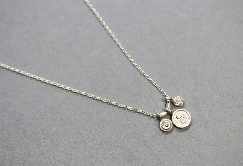 May include: A silver chain necklace with three silver charms. The charms are round and have different designs. The necklace is on a gray background.