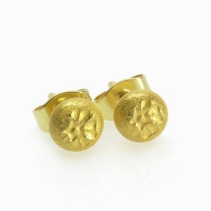 May include: A pair of gold stud earrings with a textured, circular design. The earrings are made of a shiny, metallic gold.