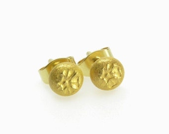 May include: A pair of gold stud earrings with a textured, circular design. The earrings are made of a shiny, metallic gold.