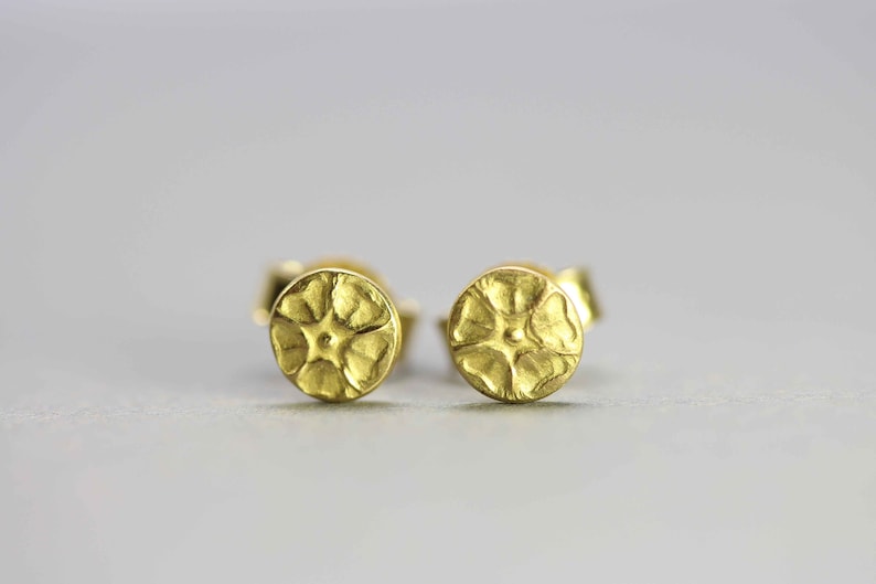 May include: A pair of gold flower-shaped stud earrings. The earrings are small and delicate, with a textured surface.