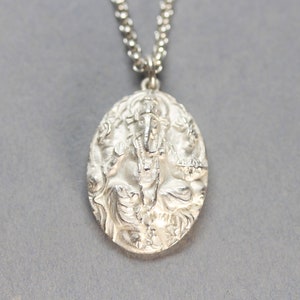 May include: Silver pendant necklace featuring a detailed, embossed image of the Hindu deity Ganesha. The pendant is oval shaped and hangs from a silver chain.