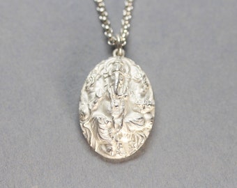 May include: Silver pendant necklace featuring a detailed, embossed image of the Hindu deity Ganesha. The pendant is oval shaped and hangs from a silver chain.