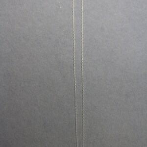 May include: A silver chain necklace with three small silver charms hanging from it. The charms are round and have different designs.