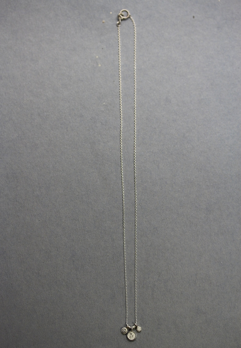 May include: A silver chain necklace with three small silver charms hanging from it. The charms are round and have different designs.