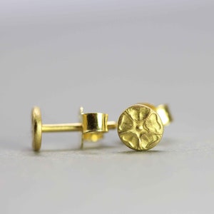 May include: A pair of gold stud earrings with a textured, circular design. The earrings are small and delicate.