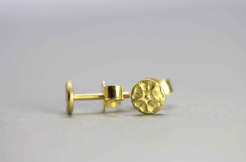 May include: A pair of gold stud earrings with a textured, circular design. The earrings are small and delicate.