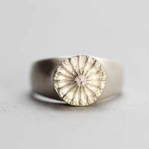 May include: A silver ring with a textured circular design on the top.