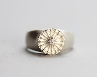 May include: A silver ring with a textured circular design on the top.
