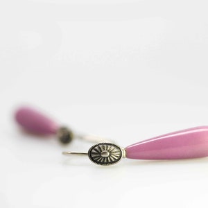 Op de afbeelding: Een paar roze druppelvormige oorbellen met zilveren accenten. De oorbellen hebben een delicaat ontwerp en zijn perfect om elke outfit een vleugje elegantie te geven.