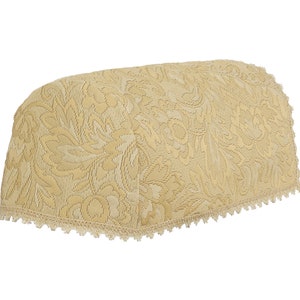Op de afbeelding: Een beige stoffen stoelhoes met een bloemenpatroon en een witte kantversiering.