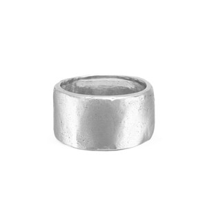 Pode incluir: Um anel de banda larga em prata com uma superfície texturizada e irregular. O metal tem um acabamento mate e escovado com subtis reentrâncias e uma borda ligeiramente irregular, conferindo à peça um aspeto cru e orgânico.