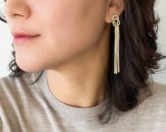 May include: A pair of gold dangle earrings with a knotted design and multiple chains hanging down.