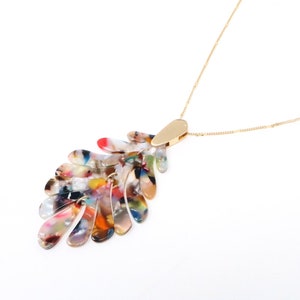 May include: A gold chain necklace with a multi-colored, abstract leaf-shaped pendant. The pendant is made of a translucent material with swirls of red, orange, yellow, green, blue, and purple.