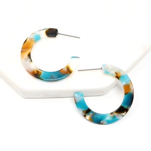 May include: A pair of turquoise, brown and white patterned hoop earrings. The earrings are made of thick, rounded plastic.