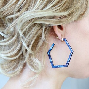 May include: A pair of blue hexagonal hoop earrings. The earrings are made of a translucent material with a marbled pattern.
