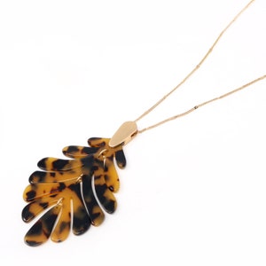 May include: A gold chain necklace with a large, brown and black tortoise shell leaf pendant.