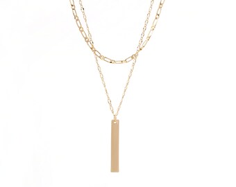 Puede incluir: Un collar de cadena dorada de dos capas con un colgante rectangular largo.