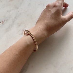 Close-up of a wrist wearing the textured gold knot cuff bracelet on a marble surface.