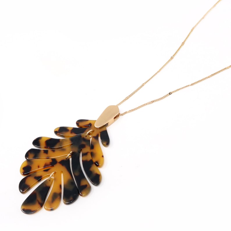 May include: A gold chain necklace with a large, brown and black tortoise shell leaf pendant.