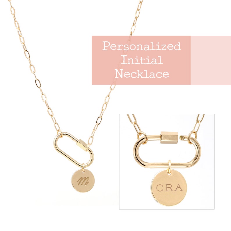 May include: A gold chain necklace with a personalized initial charm. The charm is attached to a carabiner-style clasp. The necklace is shown with the initial "M" and "CRA".